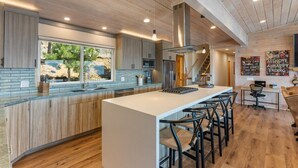 Une cuisine moderne dotée d’un îlot central, de meubles en bois et d’une grande fenêtre donnant sur un espace paysager aménagé.