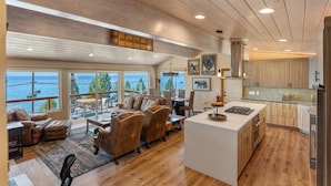 Un vaste espace de vie avec une grande fenêtre donnant sur l’océan, un coin salon confortable avec des canapés en cuir et une cuisine moderne dotée de meubles en bois.