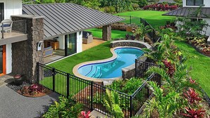 A modern house with a swimming pool, stone pillars, and lush landscaping.