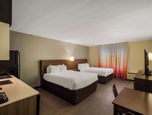 Ett hotellrum med två sängar, ett skrivbord, en tv och ett litet kök.