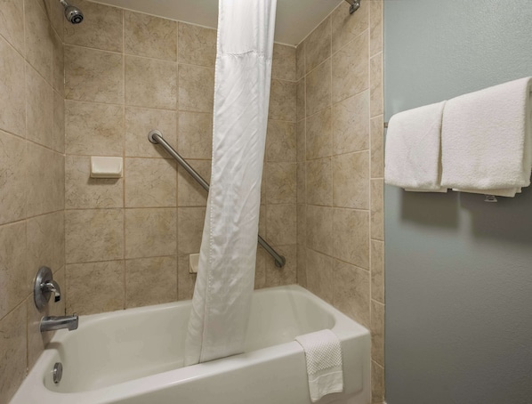 Un baño con bañera, cortina de ducha, barra de apoyo y toallero con toallas.