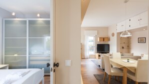 A modern hotel room with a bed, a desk, and a dining area with chairs and a table.