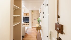 A hallway with a wooden floor, a white door with a lock, and a small table with a vase and a plant.