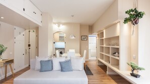 A modern hotel room with a large bed, built-in shelving, a hanging plant, and a view into the kitchen area.