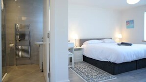 Moderni hotellihuone, jossa on suuri sänky, yöpöydät, yövalaisin, suihkutila ja kuviollinen matto.