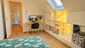 Une chambre à coucher avec un puits de lumière, un bureau, une chaise, un lit, une télévision, un vase de fleurs et une bibliothèque.