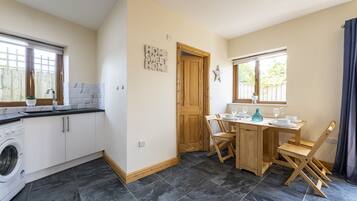 A compact kitchen with a washing machine, a dining area with a wooden table and chairs, and a wooden door.