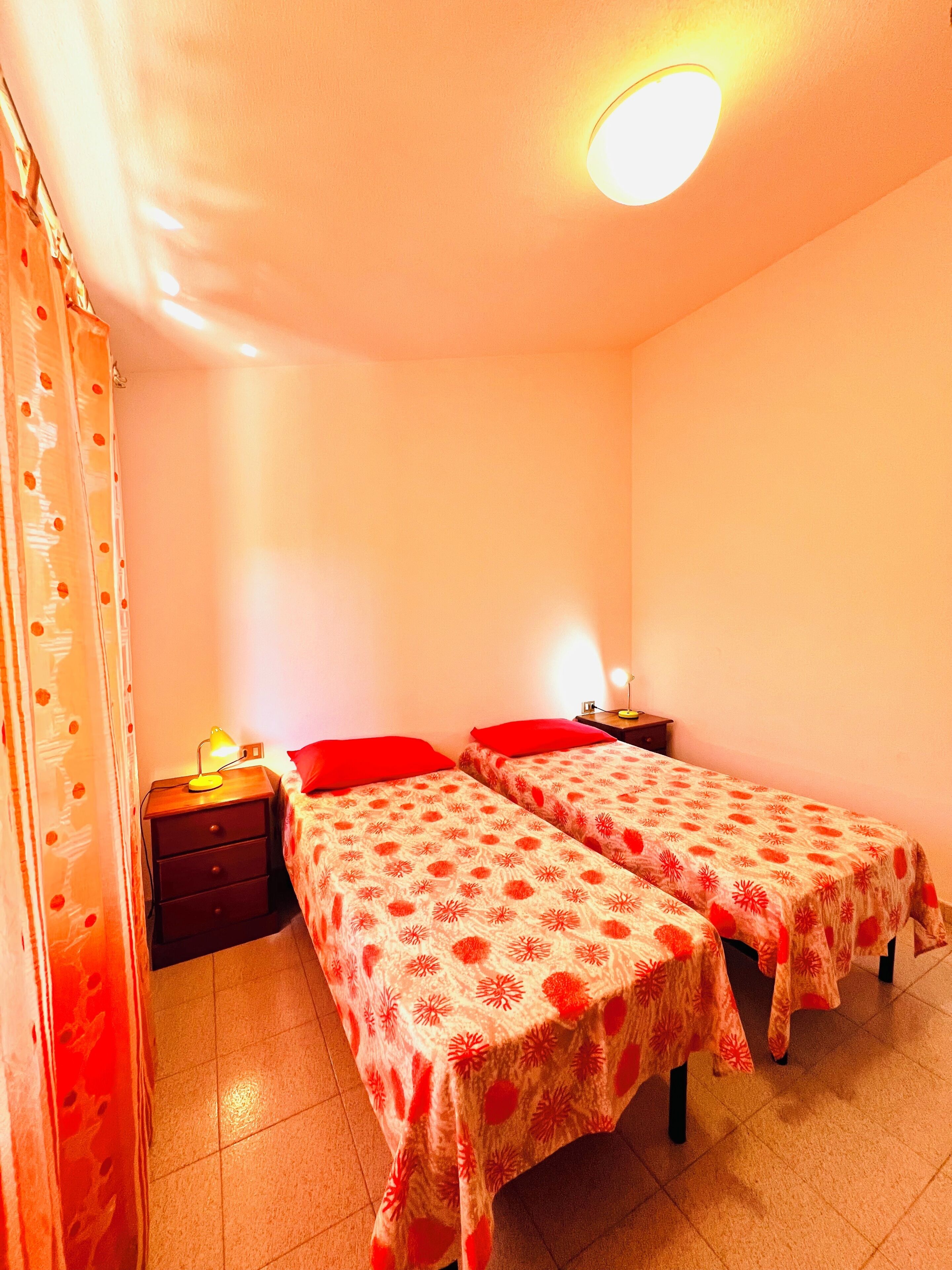 A room with two single beds, a nightstand with a lamp, and a curtain with a polka dot pattern.