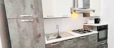 A modern kitchen with grey cabinets, a stainless steel sink, a gas stove, and a black coffee machine.
