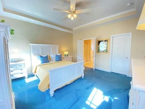 A bedroom with a large bed, a ceiling fan, and a door leading to another room.