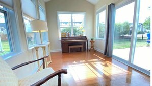 Ein geräumiges Zimmer mit einem Klavier, einem Sessel und großen Fenstern.
