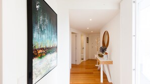 A hallway with a wooden floor, a white door, and a painting on the wall.
