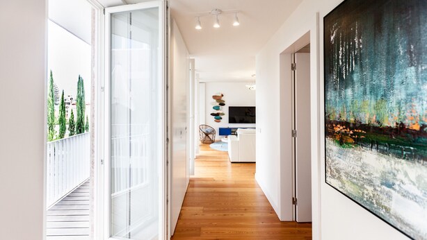 A modern interior with a wooden floor, a large painting on the wall, and a glass door leading to an outdoor area.