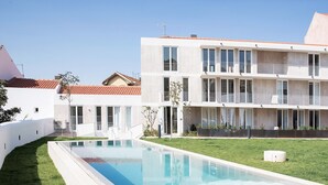 A modern building with a swimming pool, flat roof, and multiple balconies.
