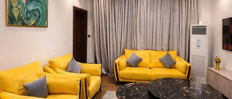 A modern living room with yellow sofas, a round black coffee table, and a chandelier.