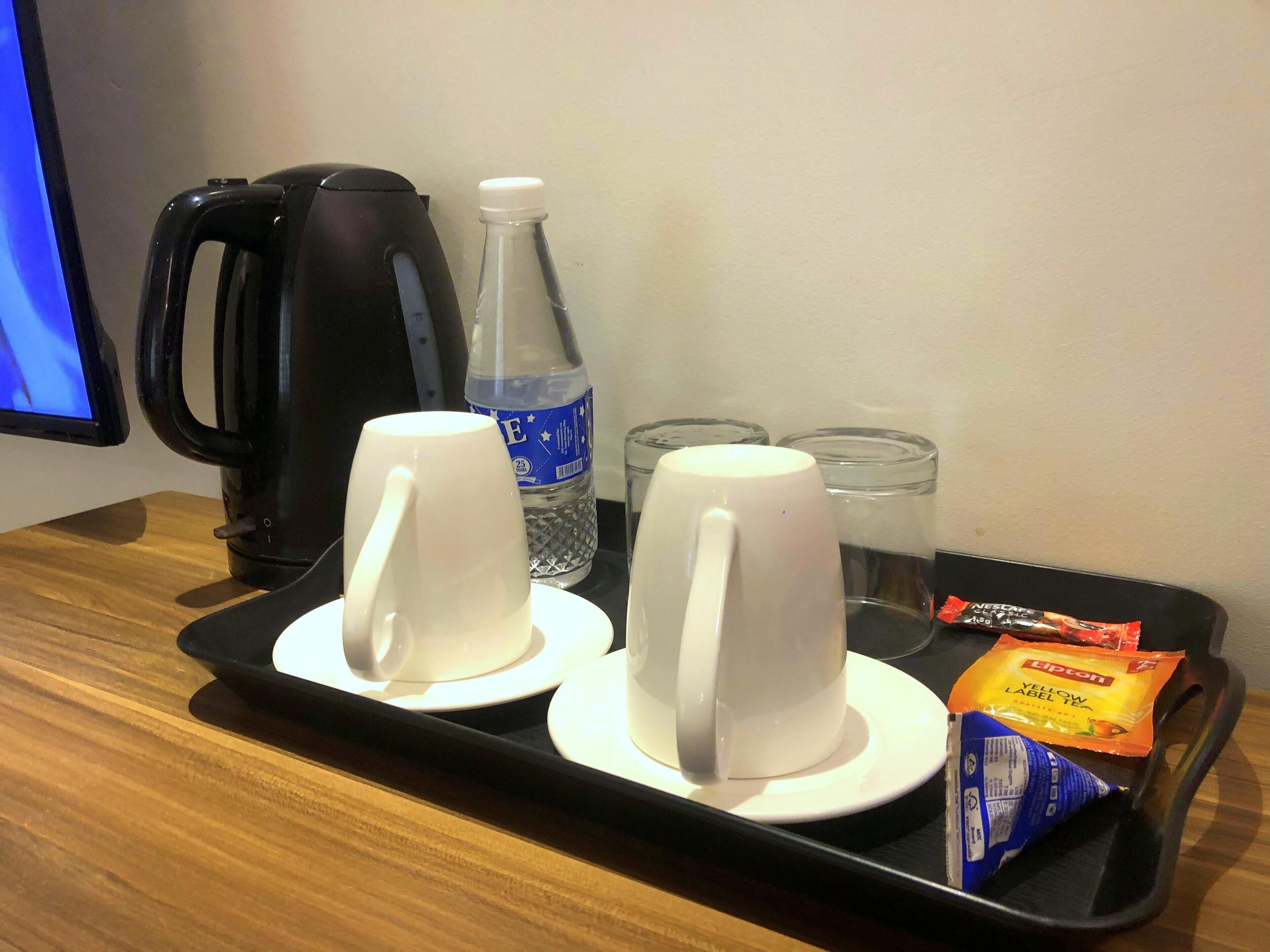 A tray with two white mugs, a water bottle, a glass, and a packet of Lipton tea on a wooden table.