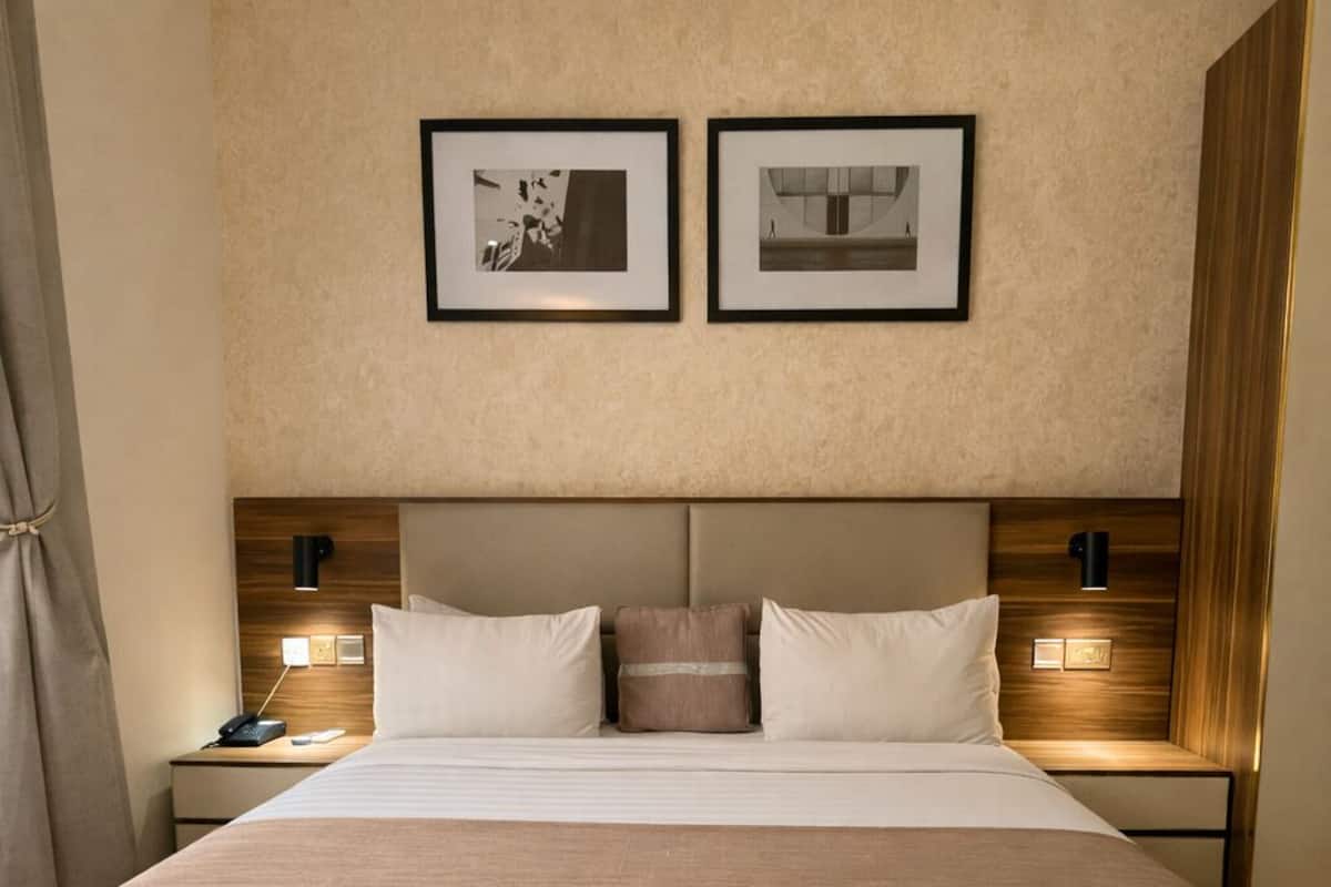 A hotel room with a large bed, two bedside tables, a headboard, and two framed pictures on the wall.