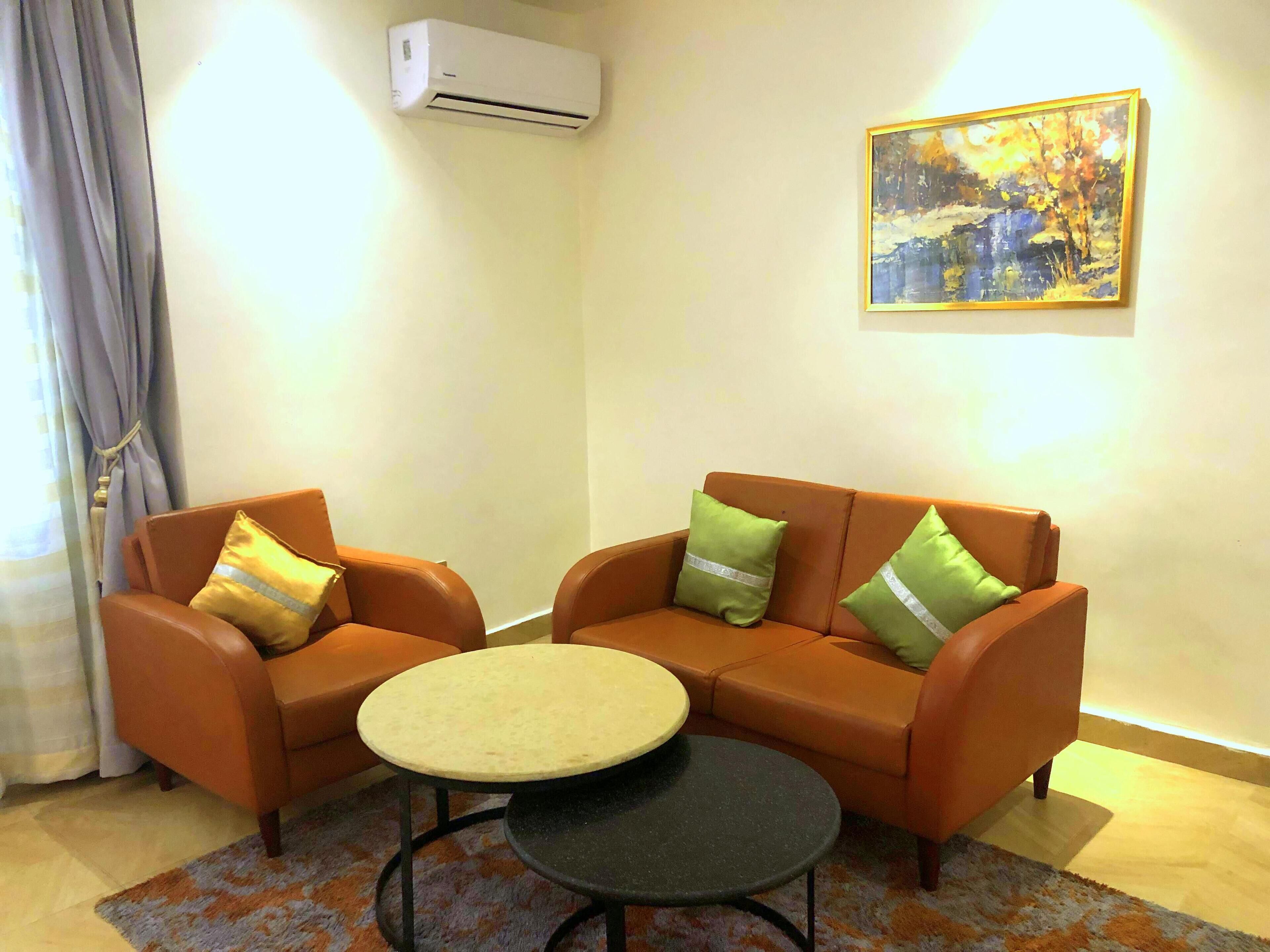 Un salon avec deux canapés orange, une table ronde, un tableau accroché au mur et un climatiseur.