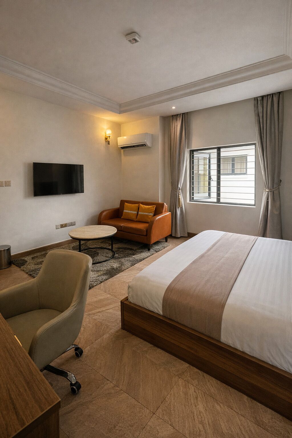 Habitación de hotel con cama, sofá, sillón, mesita, televisor y aire acondicionado.