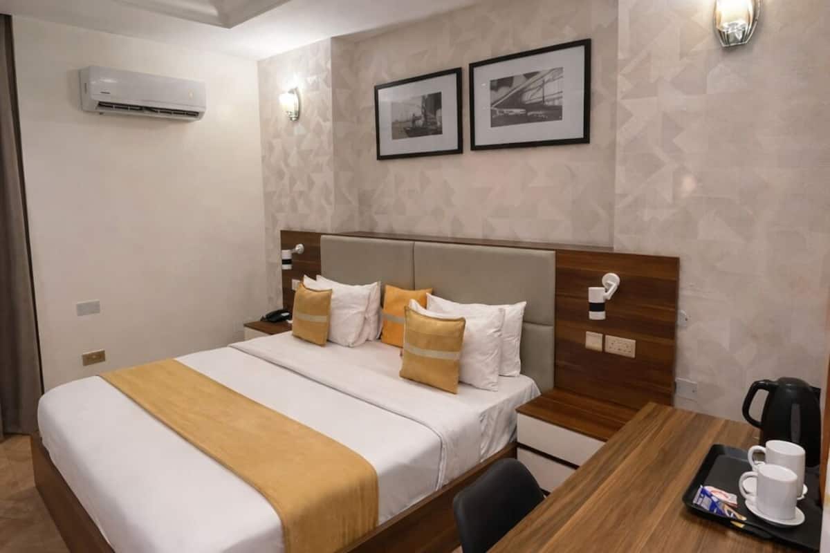 A hotel room with a bed, bedside table, desk, and wall-mounted air conditioning unit.