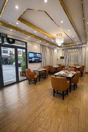 A hotel dining area with tables, chairs, a chandelier, a television, and an exit sign. - Caritas Inn Lekki (Lekki)