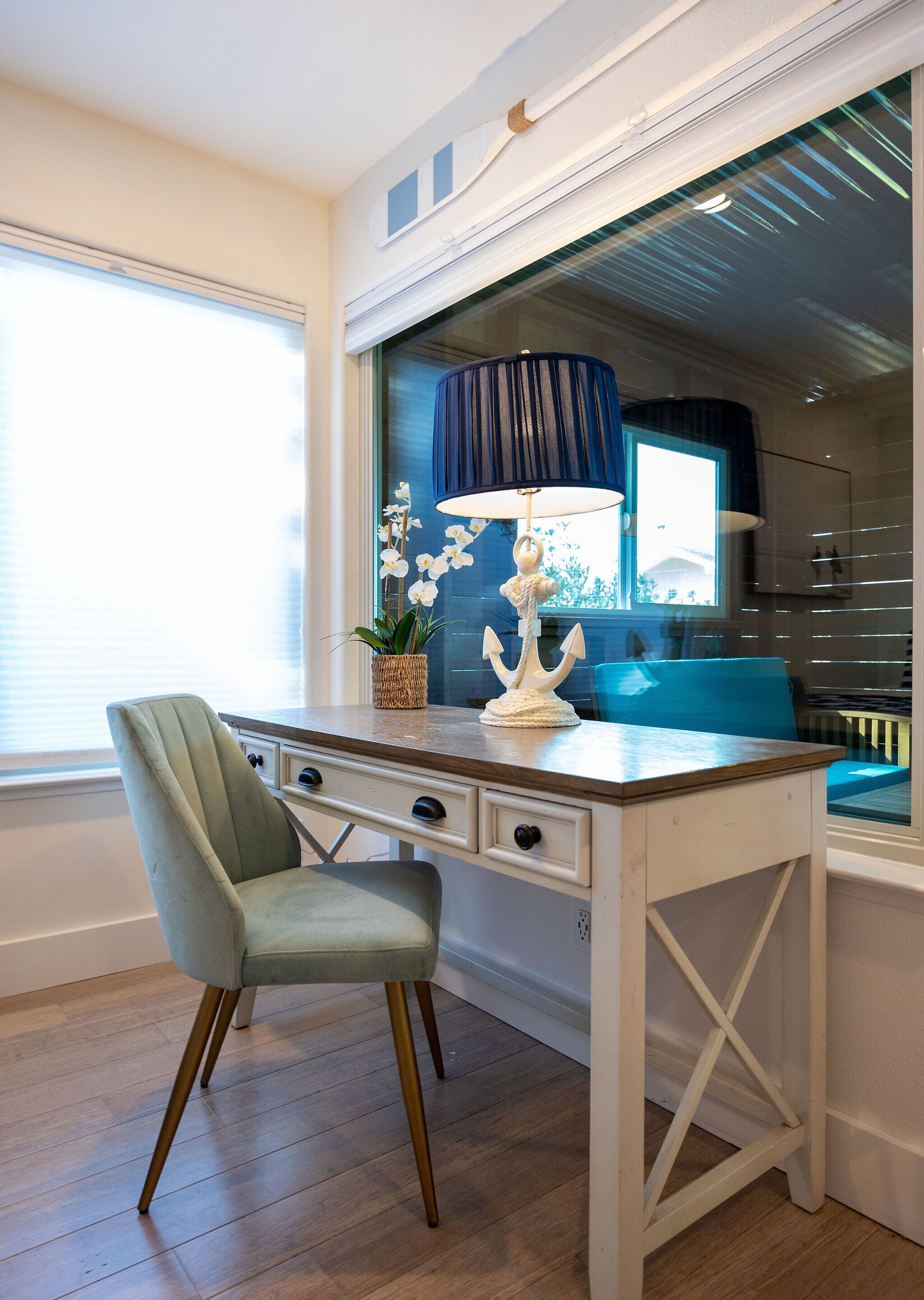 A dining area with a white table, a green chair, a blue lamp, and a view of the outdoors through a window.