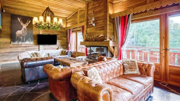A log cabin interior with a leather sofa, a television, a fireplace, and deer antlers on the wall.