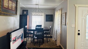 Un comedor con una mesa y sillas, una araña, un tapete estampado y obras de arte enmarcadas en las paredes.