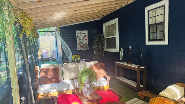 Un área de estar al aire libre con techo, muebles de madera, un letrero de bienvenida y una ventana.