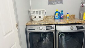 Un área de lavandería con dos lavadoras Maytag de carga frontal, una cesta blanca y botellas de detergente sobre una encimera de granito.