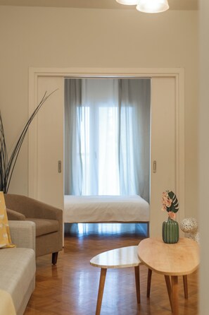 A cozy room with a bed, a sofa, a small table, and a vase with flowers. - Houseloft Queen Olga Casa (Thessaloniki)