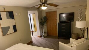 Een hotelkamer met een bed, een bureau, een stoel, een televisie en een plafondventilator.