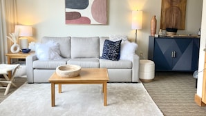 Een woonkamer met een bank, een salontafel, een lamp en een schilderij aan de muur.