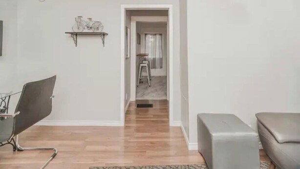 A modern living room with a wooden floor, a grey sofa, a grey ottoman, a metal chair, and a wall-mounted shelf with a bicycle model. - Red Roof Rental (Thunder Bay)