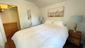 A bedroom with a bed, a nightstand, a lamp, a painting, and a wardrobe. - Red Roof Rental (Thunder Bay)