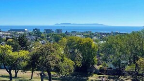 A coastal residential area with houses, trees, and a clear view of the sea and a distant mountain. - Red Roof Rental (Thunder Bay)