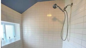 A bathroom with white tiled walls, a bathtub, and a shower with a handheld showerhead. - Red Roof Rental (Thunder Bay)