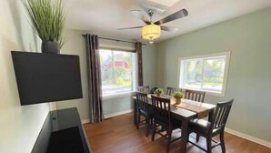 A dining area with a wooden table, chairs, a ceiling fan, and a TV mounted on the wall. - Hidden Pearl Short Term Rental (Thunder Bay)