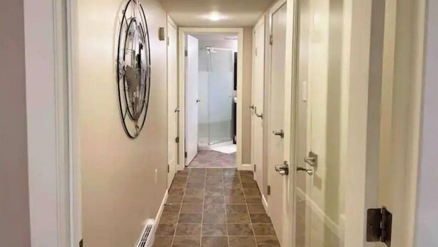 A hallway with a tiled floor, a wall-mounted abstract art piece, and a door with a metallic handle. - Hidden Pearl Short Term Rental (Thunder Bay)
