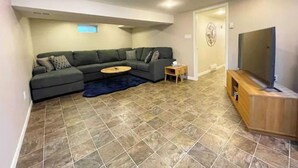 A living room with a sectional sofa, a coffee table, a TV on a wooden stand, and a patterned rug. - Hidden Pearl Short Term Rental (Thunder Bay)