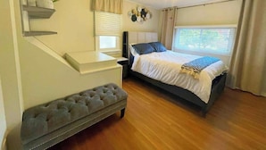 A bedroom with a bed, a bench, a ceiling fan, a window, and a plant. - Hidden Pearl Short Term Rental (Thunder Bay)