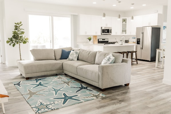 A modern living room with a sectional sofa, a starfish-patterned rug, and a kitchen in the background.