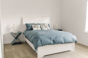 A bedroom with a white bed, teal bedding, and a decorative starfish on a wooden nightstand.
