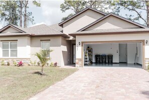 A two-story house with a garage, a small front yard with a palm tree, and a paved driveway.