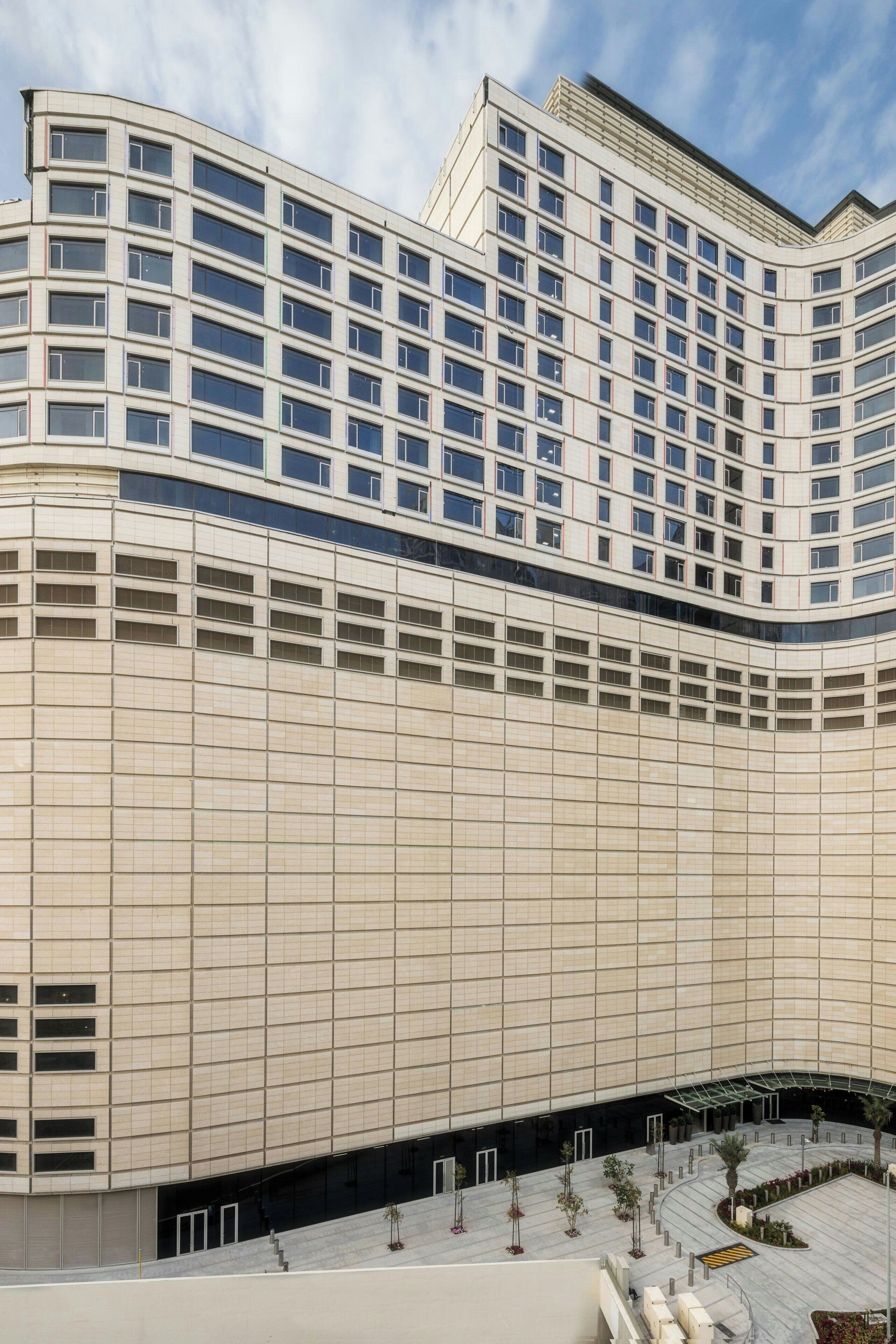 A modern hotel with a curved facade, multiple floors, and a central courtyard with seating and plants.