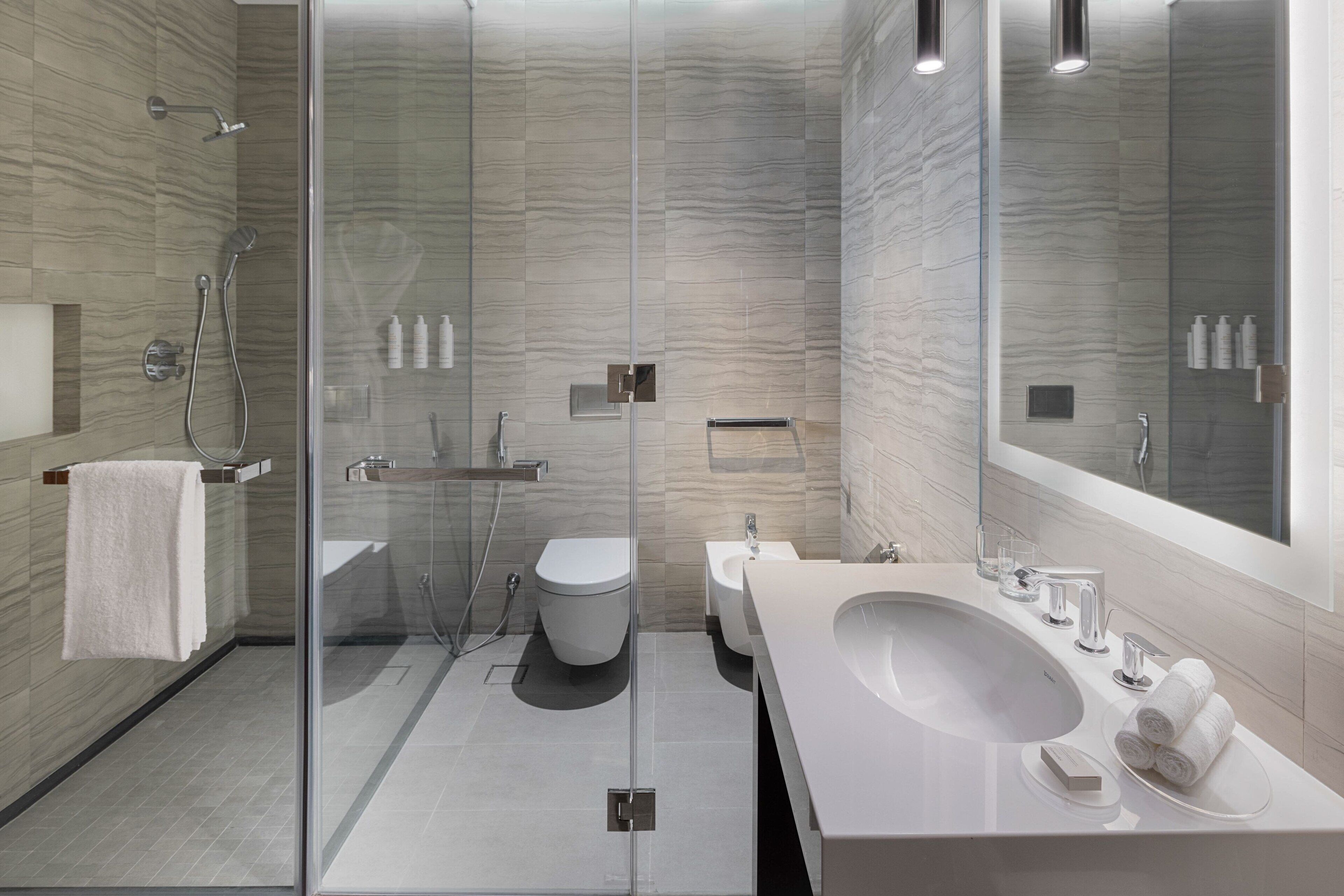 A modern bathroom with a glass-enclosed shower, a large sink, and a bidet.