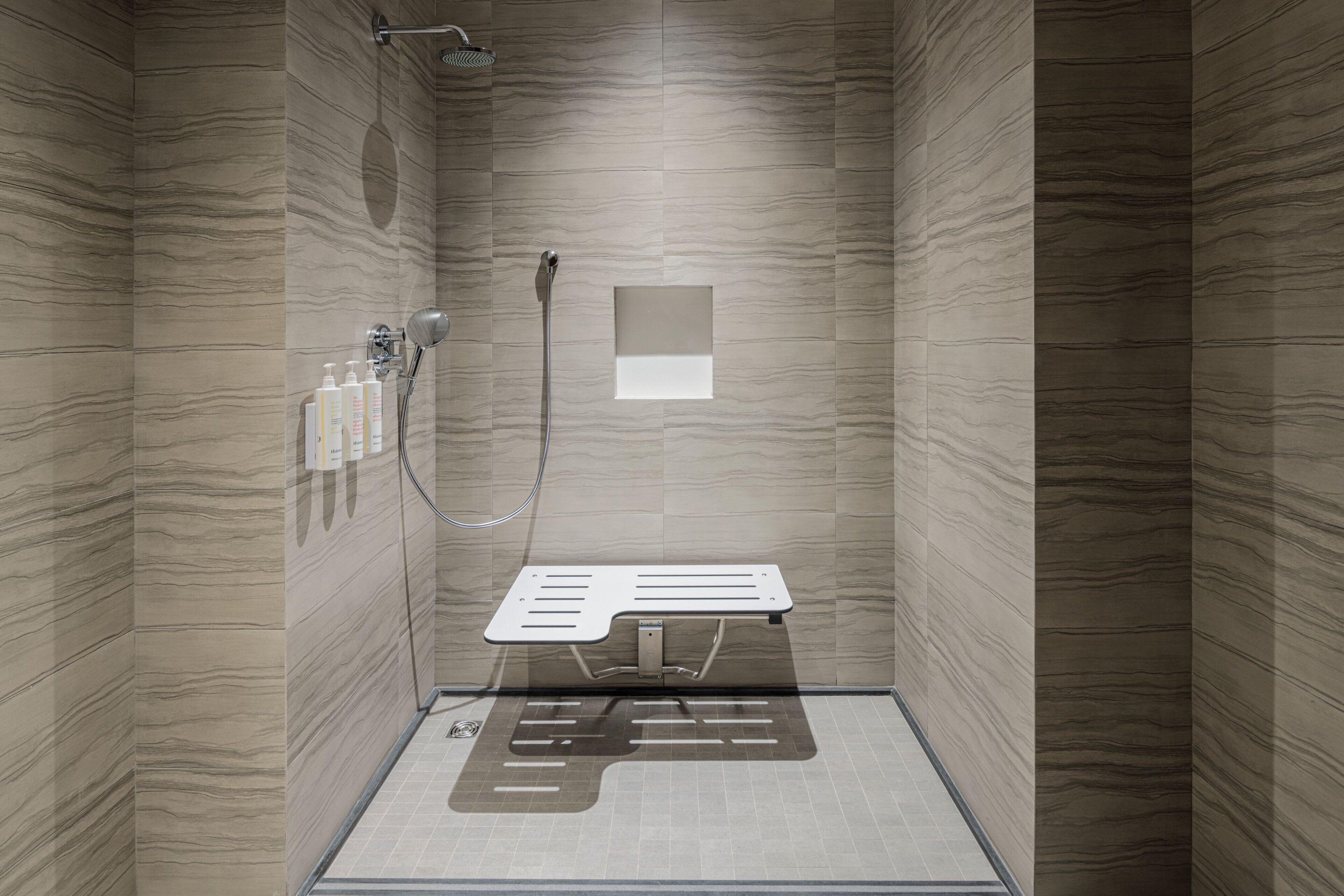 A modern shower with a built-in seat, a handheld showerhead, and a wall-mounted control panel.