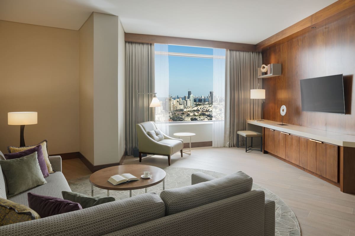 Ein modernes Hotelzimmer mit Blick auf die Stadt, einem Flachbildfernseher, einer Couch, einem Couchtisch und einer kleinen Essecke.