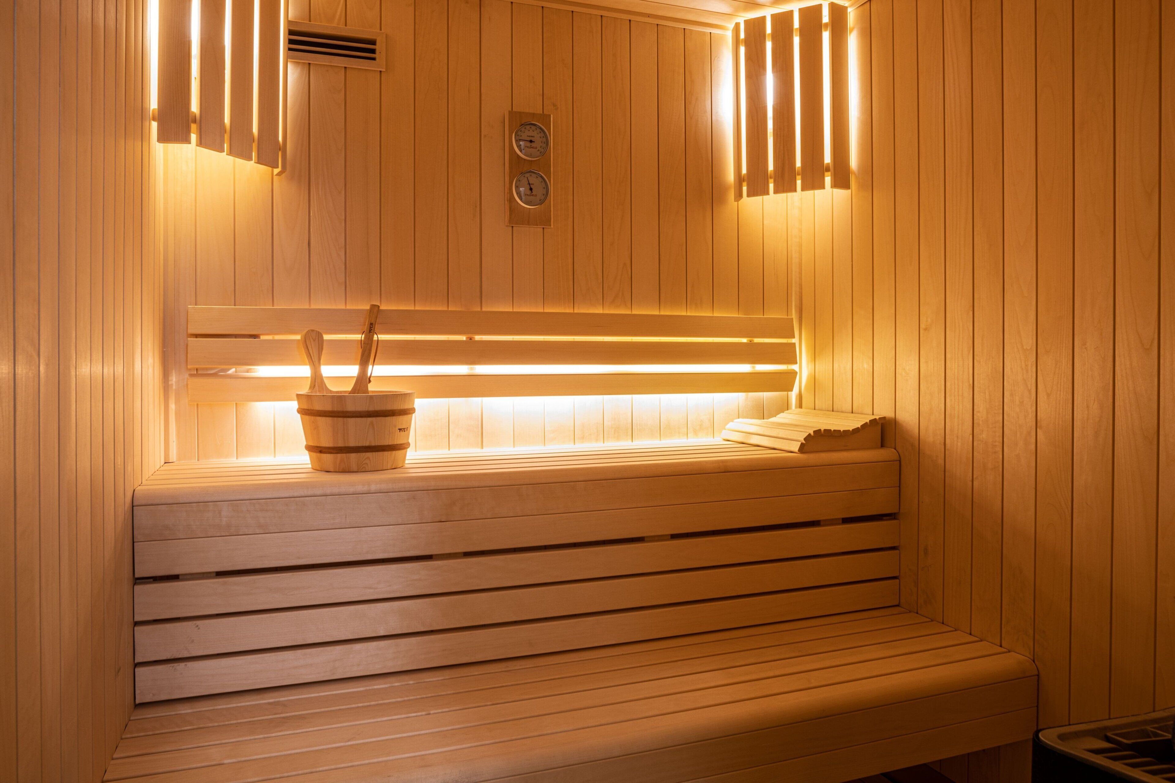 A wooden sauna bench with a bucket and a towel, and a wall-mounted heater.