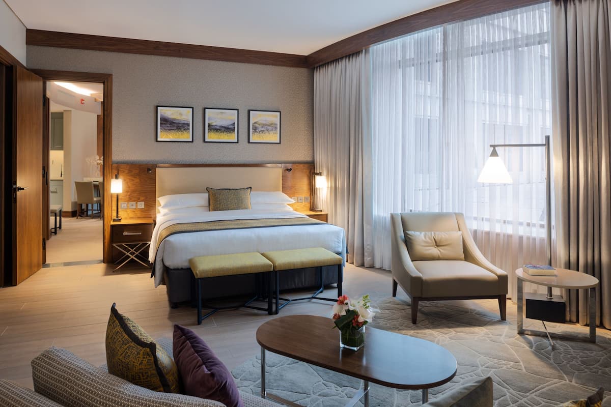 Ein Hotelzimmer mit einem großen Bett, einer Schlafcouch, einem Sessel, einem kleinen Tisch und einer Lampe.